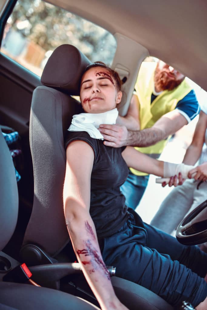 A woman who got into a car accident, she is sitting in her car unconcious. A paramedic is trying to stop the bleeding.