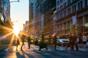 Pedestrians cross a crosswalk at sunset on a busy urban street with traffic behind them