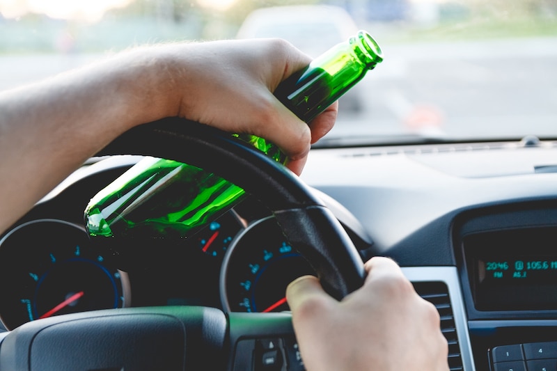 Drunk young man driving a car with a bottle of beer