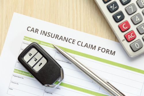 Top view of car insurance claim form with car key and calculator on wooden desk