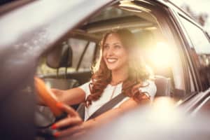 Beautiful young happy smiling woman driving her new car at sunset.