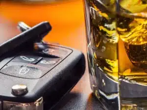 Car keys and glass of alcohol on table.