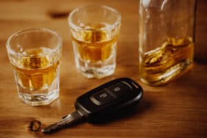 A car key on a table next to shot glasses and a bottle of alcohol