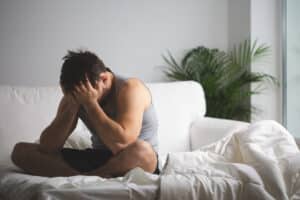 Emotionally distressed man holding his face in his hands while sitting on a couch