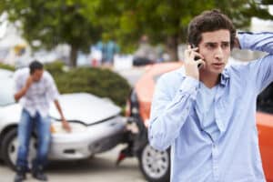 Stressed man on phone after being in a car accident, shown in background