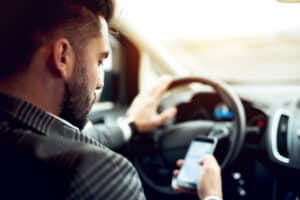 Man looks down at cell phone while driving in Boulder, CO