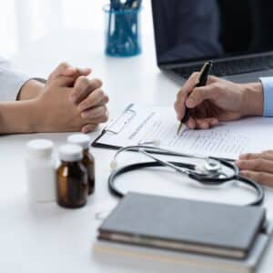 Doctor and patient sitting and talking at medical examination at hospital office, close-up