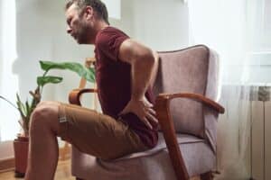 A man with a back injury sitting in a chair and holding his lower back